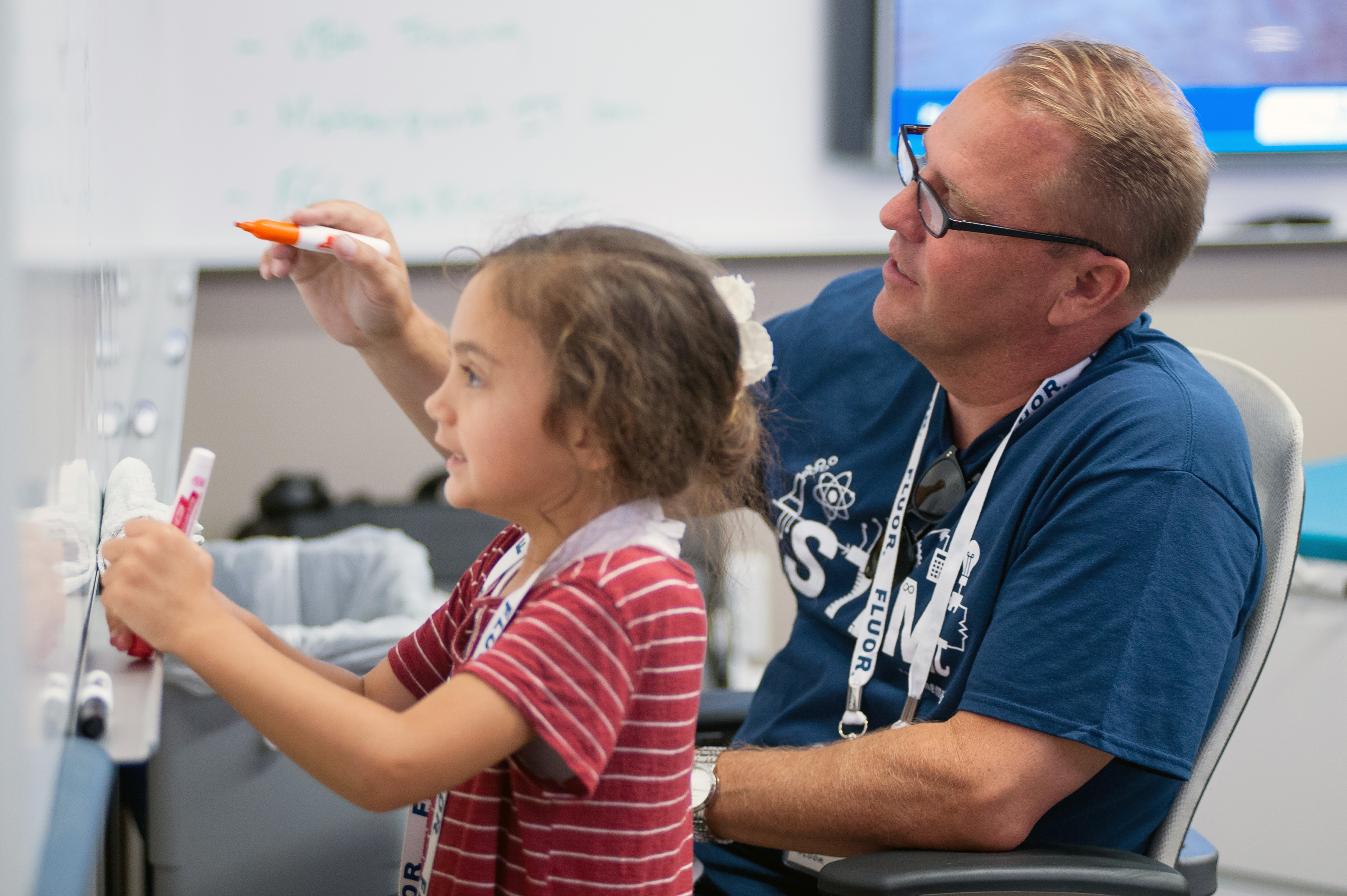 On a STEM day, a Fluor volunteer works with a girl at a dry erase board