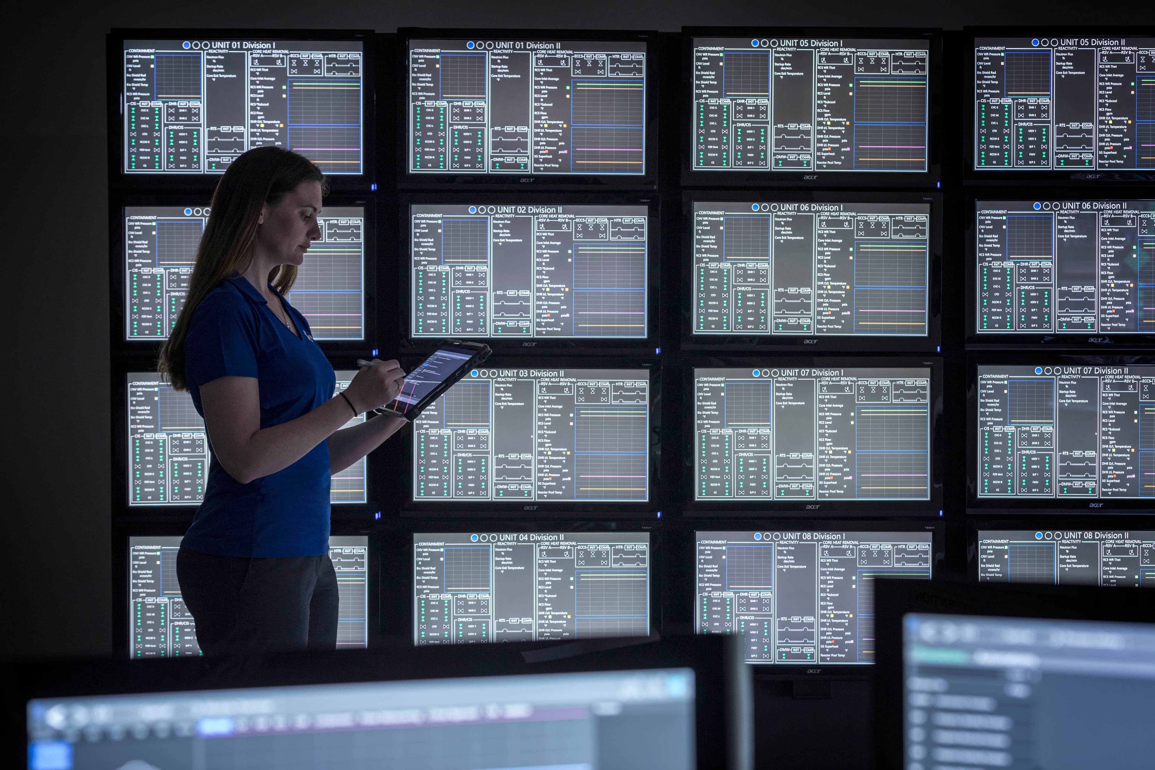 Woman in front of screens holding a tablet